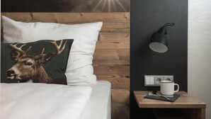 A bedroom with a wooden headboard, a bed with white bedding, a pillow with a deer image, a nightstand with a lamp, and a wall-mounted outlet. - HomeHotel Salzberg (Berchtesgaden)