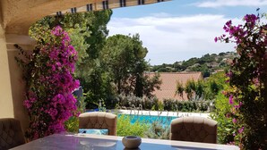 Un patio al aire libre con mesa y sillas, piscina y abundante vegetación.