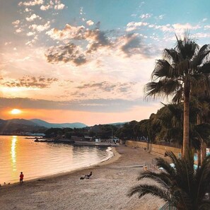 A beach with a sunset, palm trees, and a calm sea. - VILLA LES ISSAMBRES GULF OF ST TROPEZ 1KM FROM THE SEA (Les Issambres)