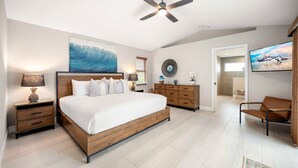 A bedroom with a large bed, wooden headboard, a ceiling fan, a TV, a wooden dresser, and a chair.