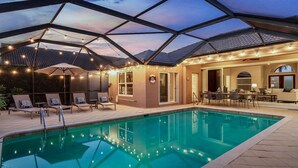 A swimming pool with a glass ceiling, lounge chairs, and a patio area with tables and chairs.