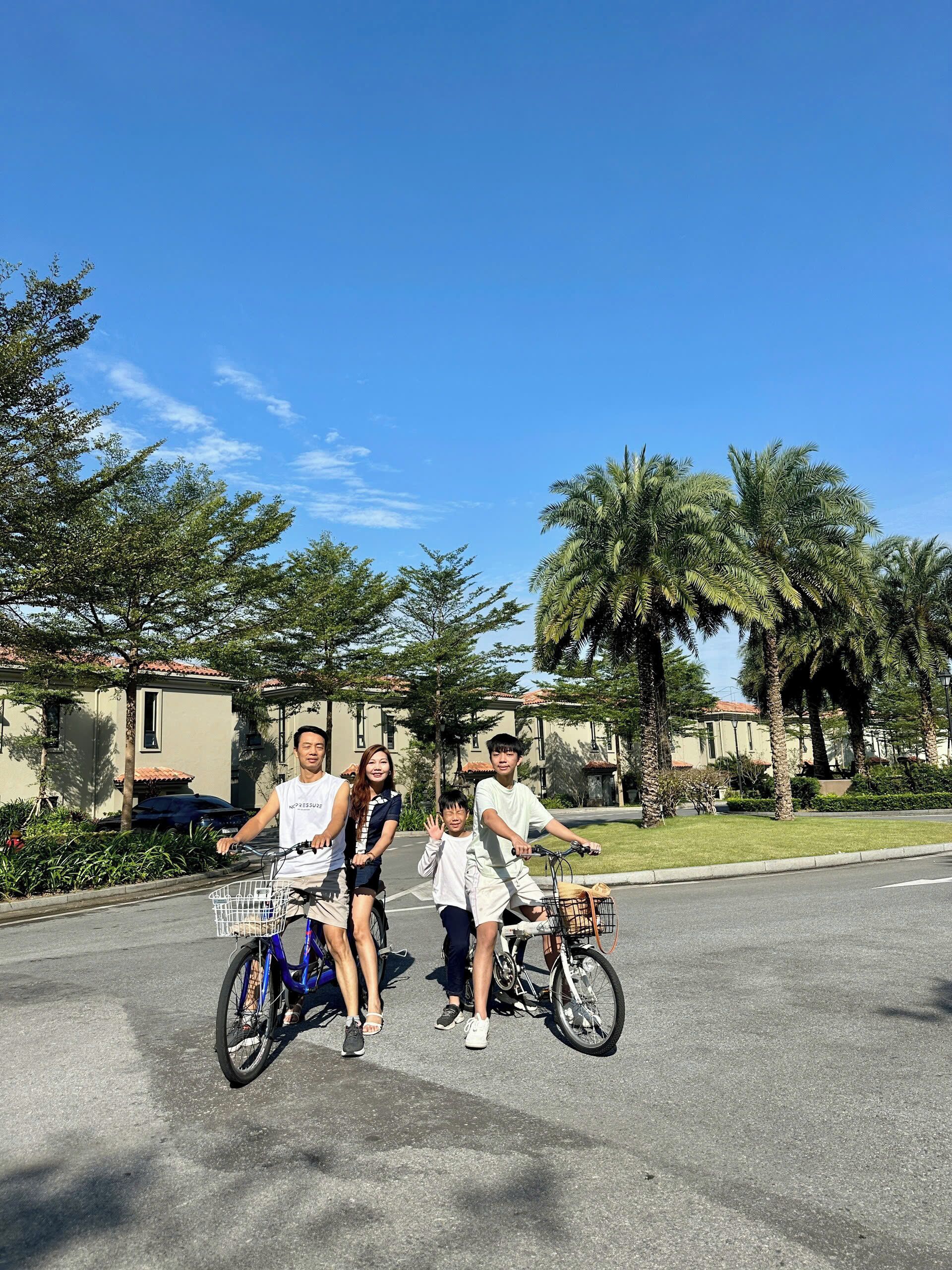 A family on bicycles in a residential area with palm trees and houses in the background.