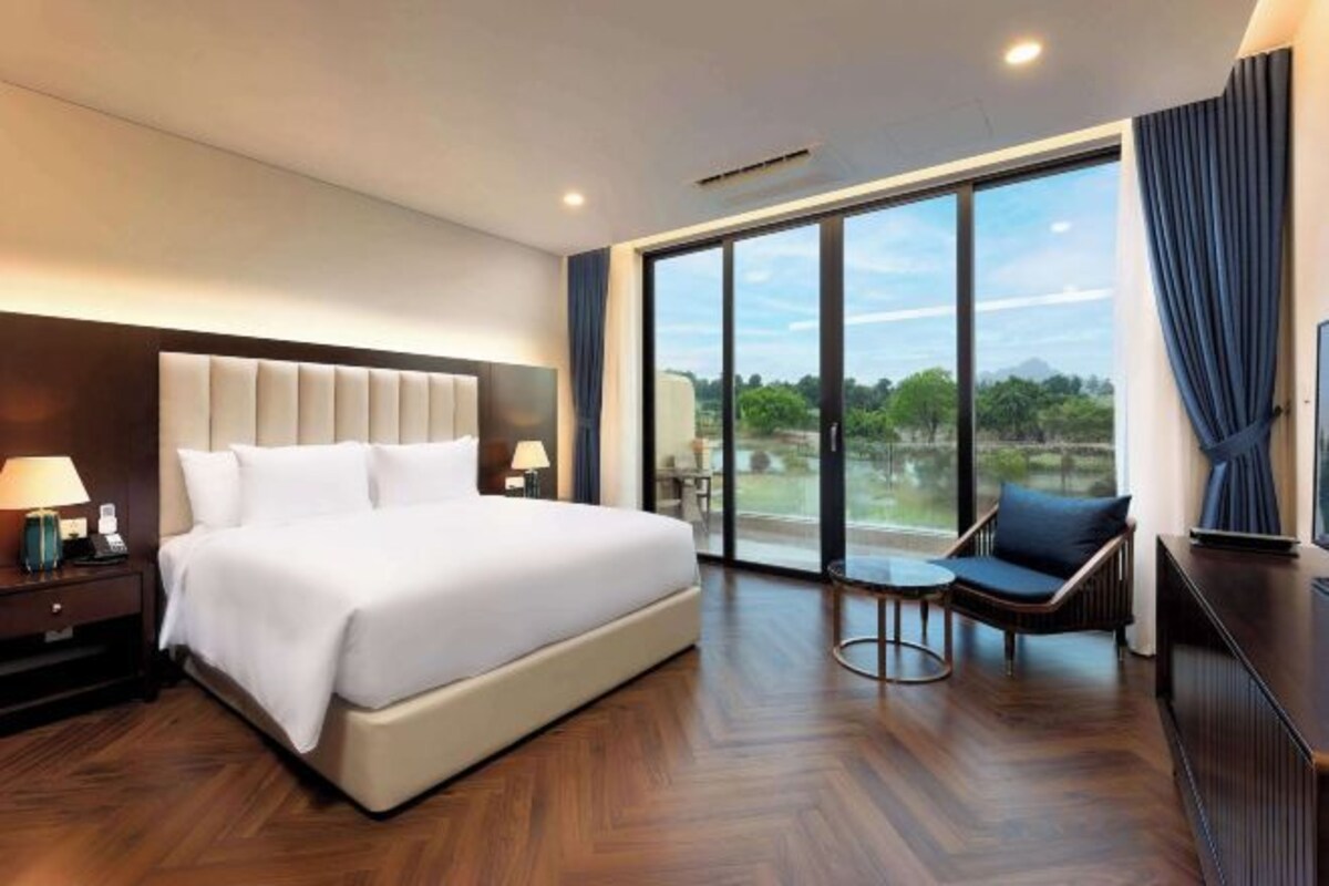 A hotel room with a large bed, a desk, a chair, and a view of the outdoors.