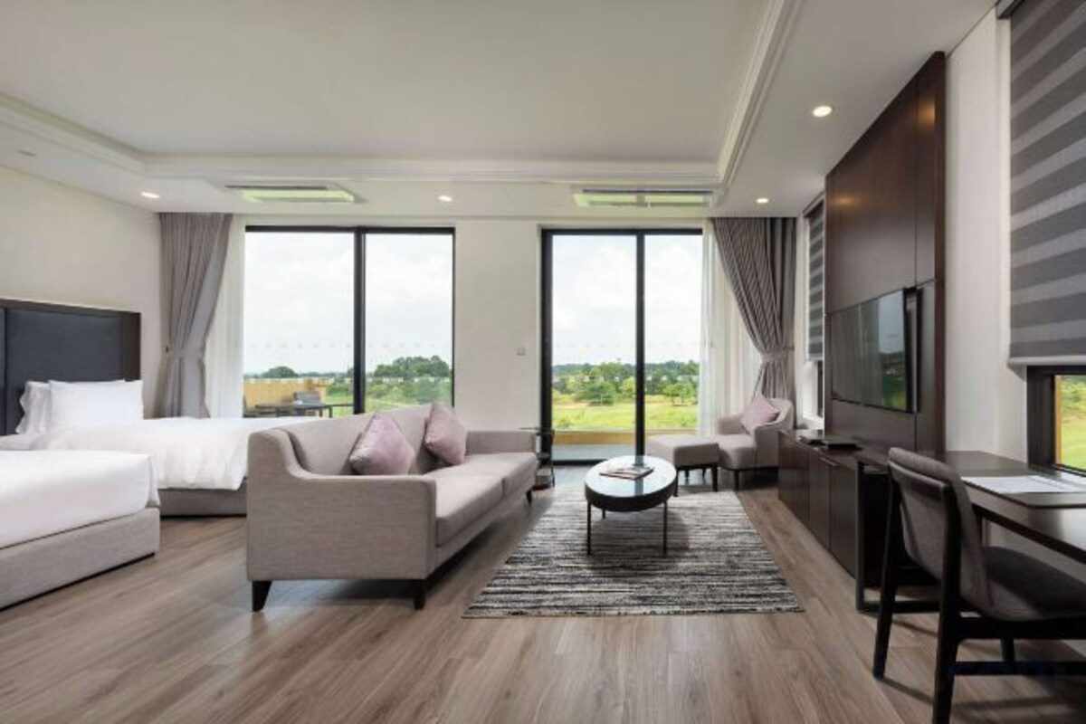 A modern hotel room with a bed, sofa, TV, and a large window.