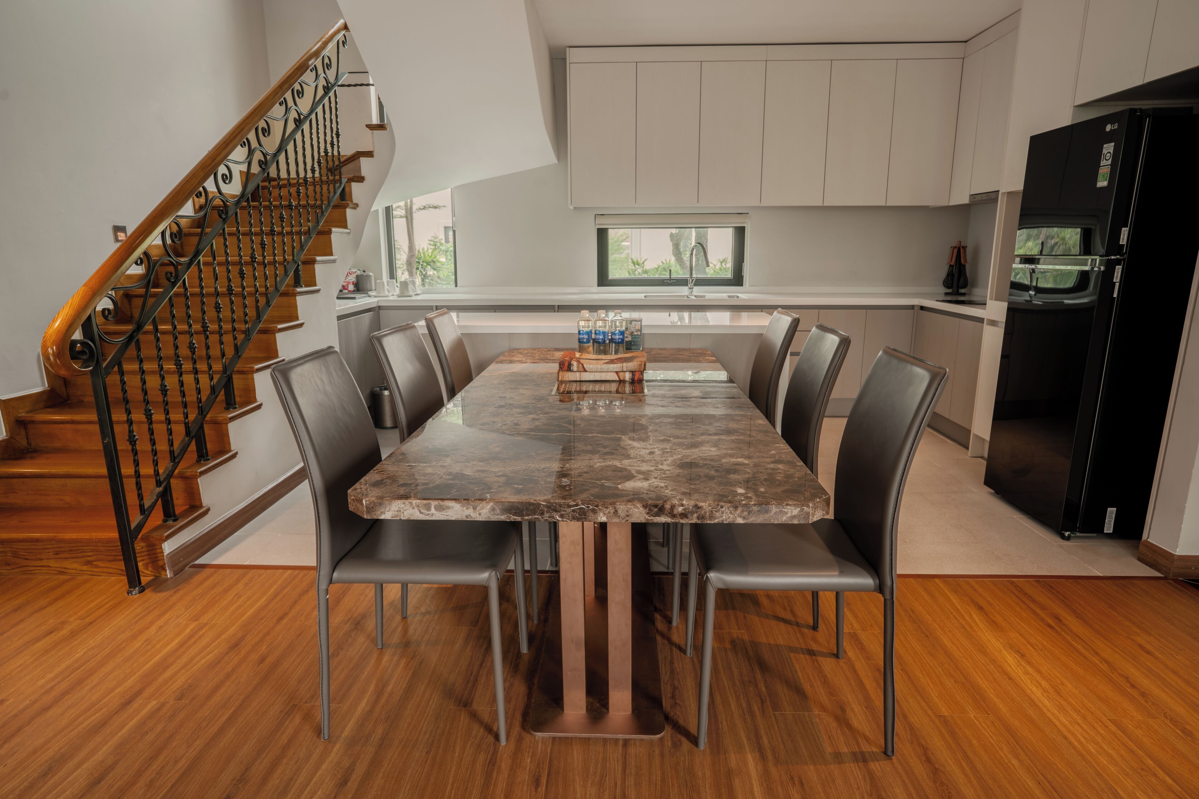 A modern kitchen with a dining table, chairs, a staircase, and a refrigerator.