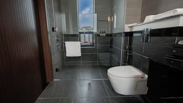 A modern bathroom with a toilet, sink, and shower area, featuring dark tiles and a visible window.