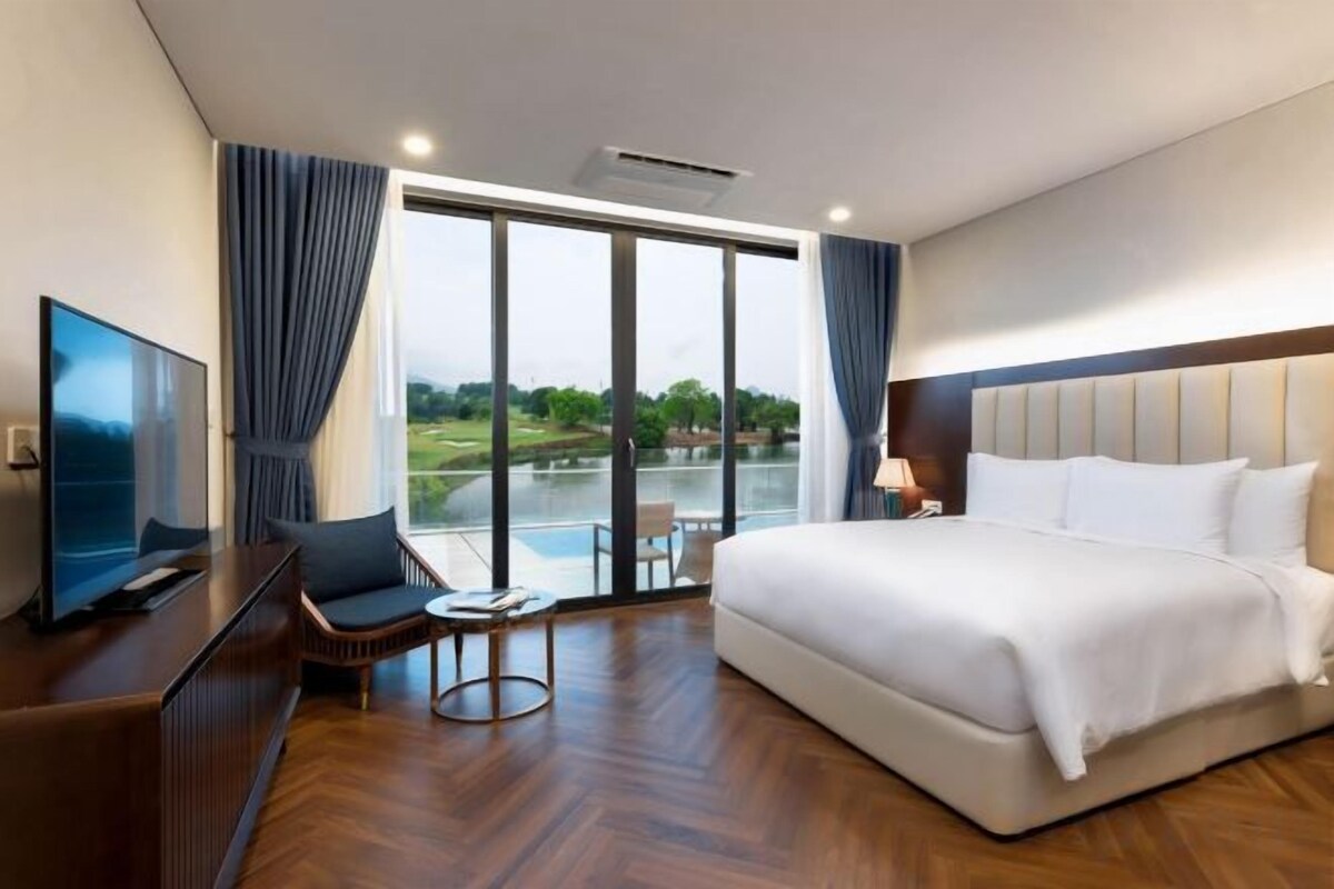 A hotel room with a large bed, a TV, a desk, and a view of a body of water.