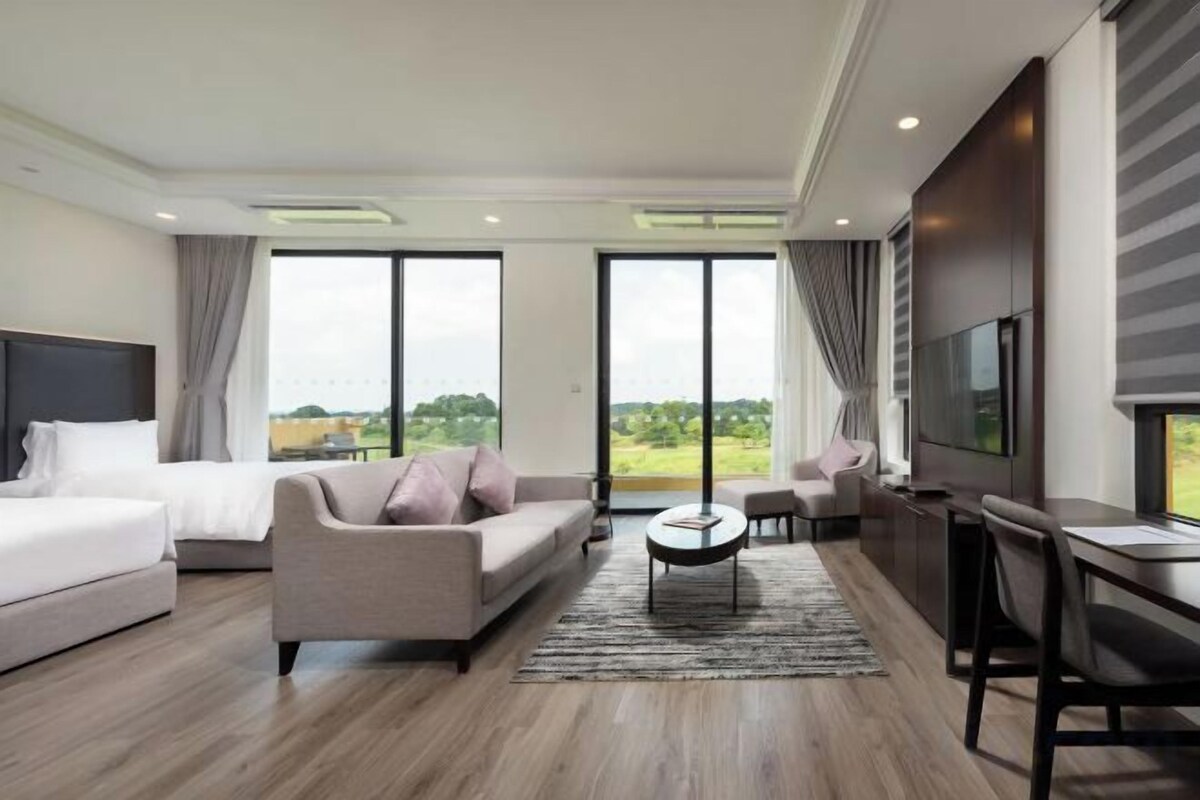 A modern hotel room with a large bed, a sofa, a coffee table, and a TV.