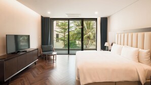 Une chambre d’hôtel moderne dotée d’un grand lit, d’une télévision, d’un coin salon et donnant sur l’extérieur grâce à une porte vitrée.