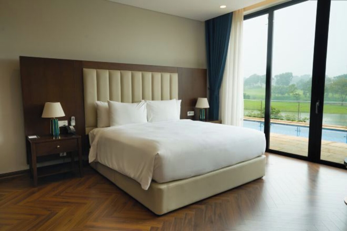 A hotel room with a large bed, two bedside tables with lamps, a view of a swimming pool through a glass door.