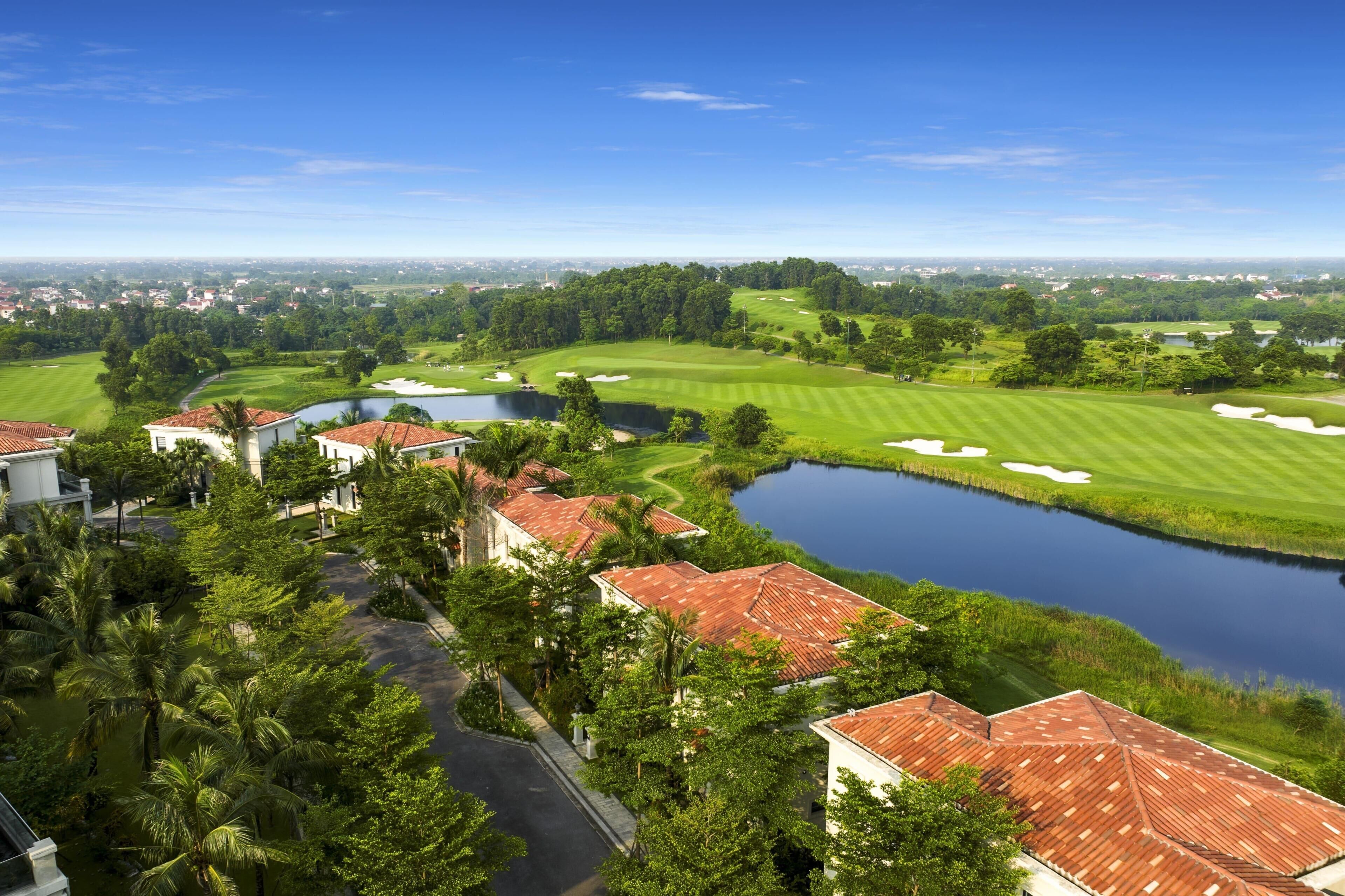 A golf course with a pond, surrounded by houses with red roofs and palm trees.