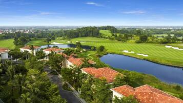 A golf course with a pond, surrounded by houses with red roofs and palm trees.
