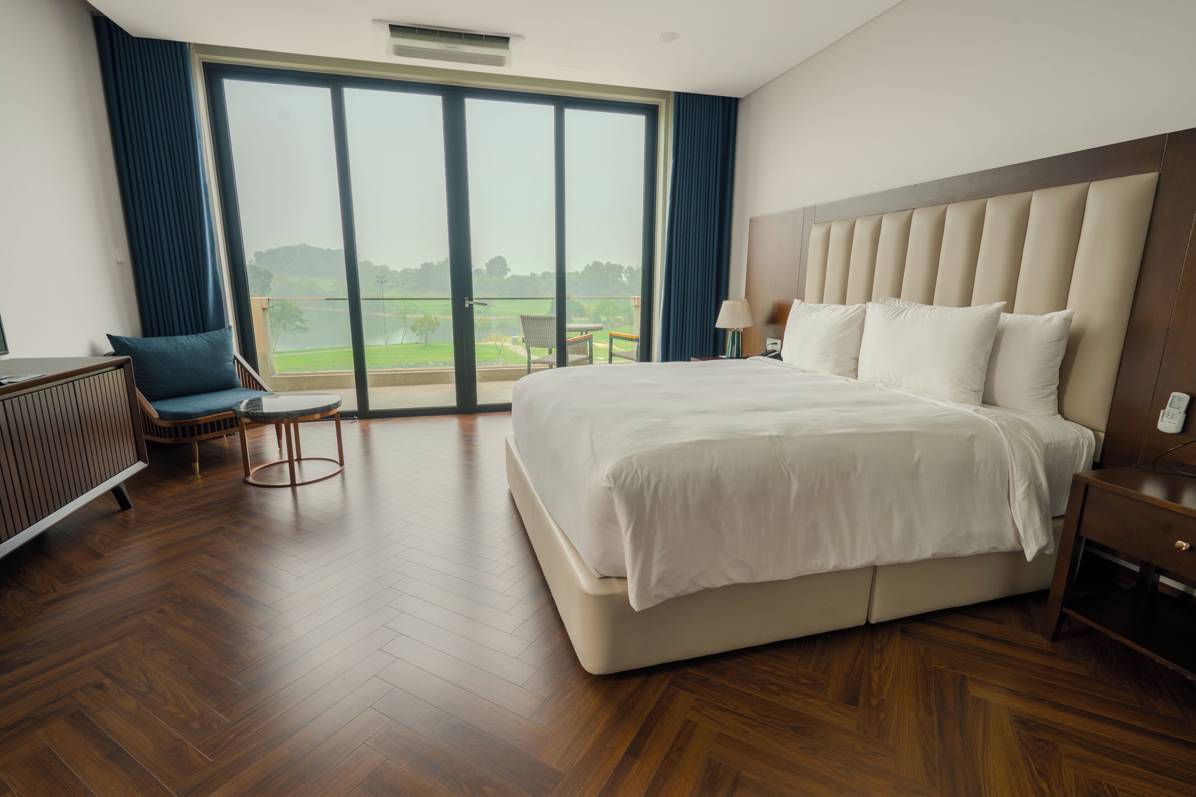 A hotel room with a large bed, a chair, a desk, and a view of the outdoors.