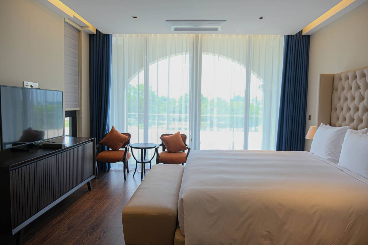 A hotel room with a large bed, a TV, a desk, and two chairs.