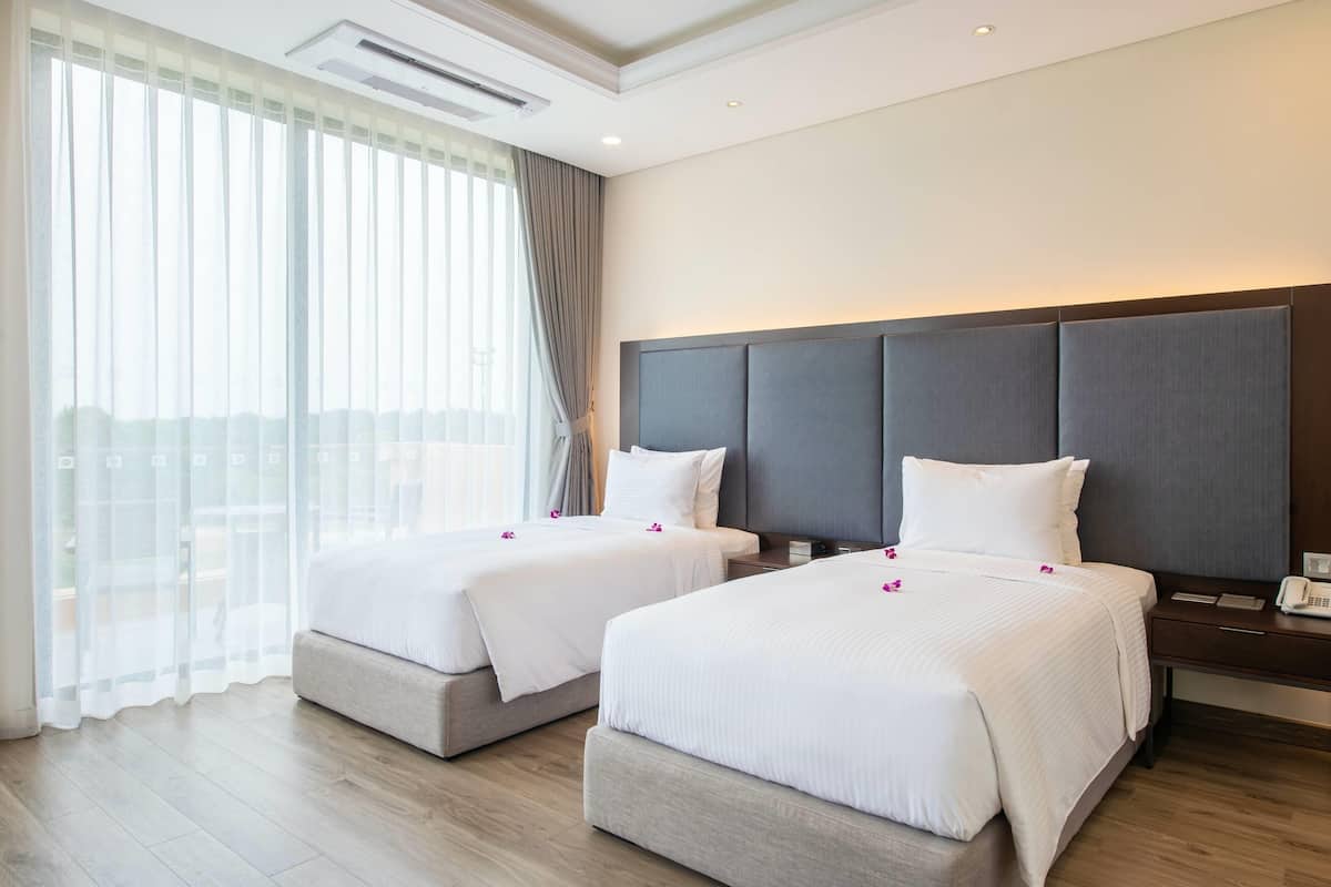 A hotel room with two beds, a large window with sheer curtains, a modern headboard, and a wooden floor.
