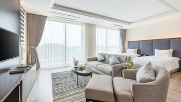 A hotel room with a bed, sofa, armchair, TV, and a small table with a vase of flowers.