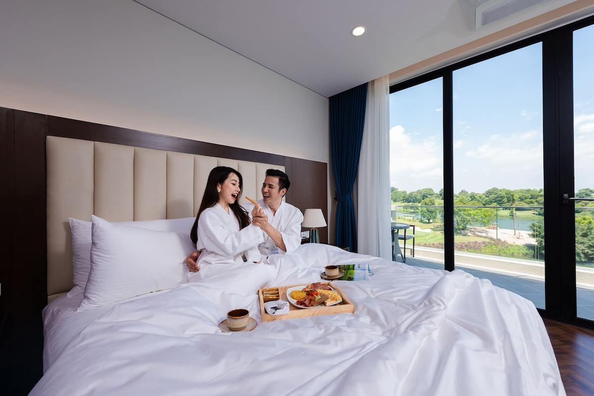 A hotel room with a large bed, a view of a golf course, and a breakfast tray on the bed.