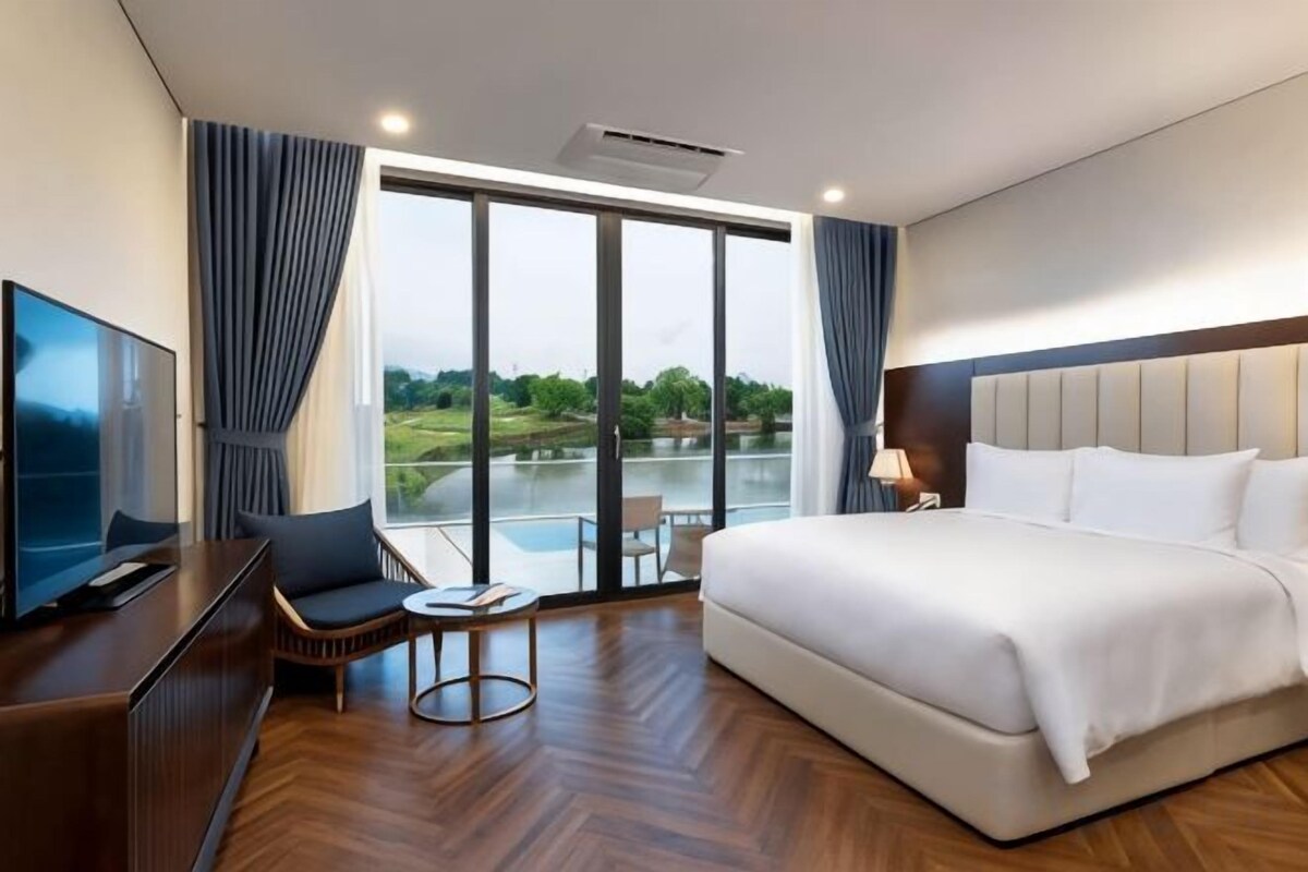 A hotel room with a large bed, a TV, a desk, and a view of a body of water.