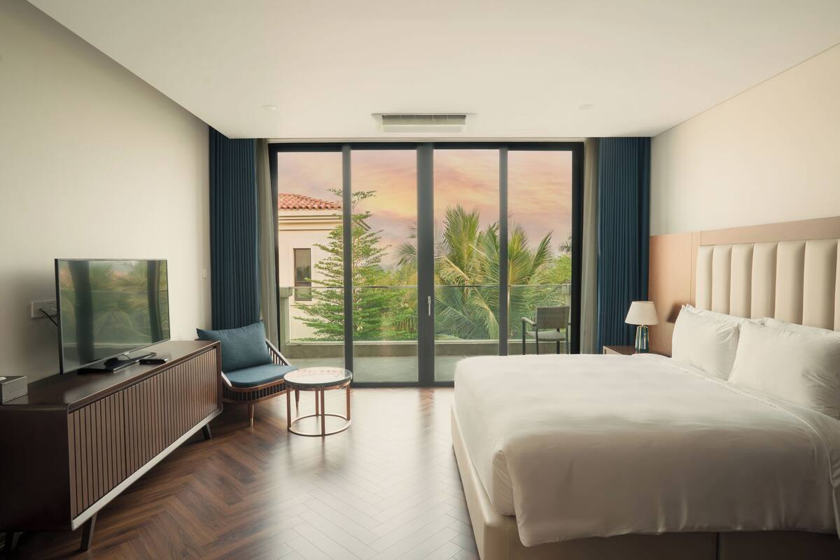A hotel room with a bed, a TV, a seating area, and a balcony with a view.
