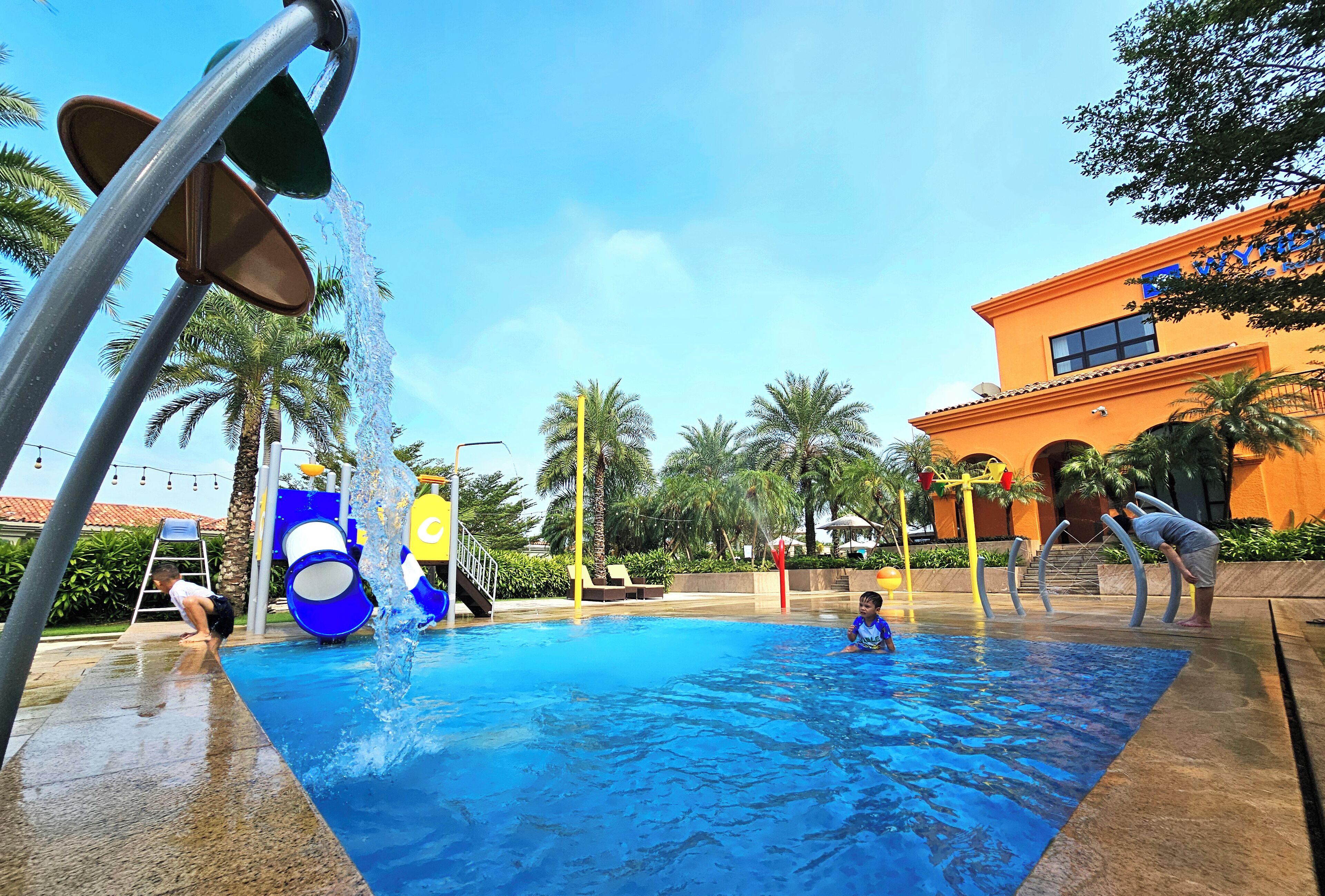 Une piscine agrémentée de jeux d’eau et bordée de palmiers.