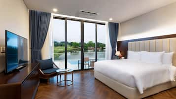 A hotel room with a large bed, a television, a small table, and a view of a golf course and lake.
