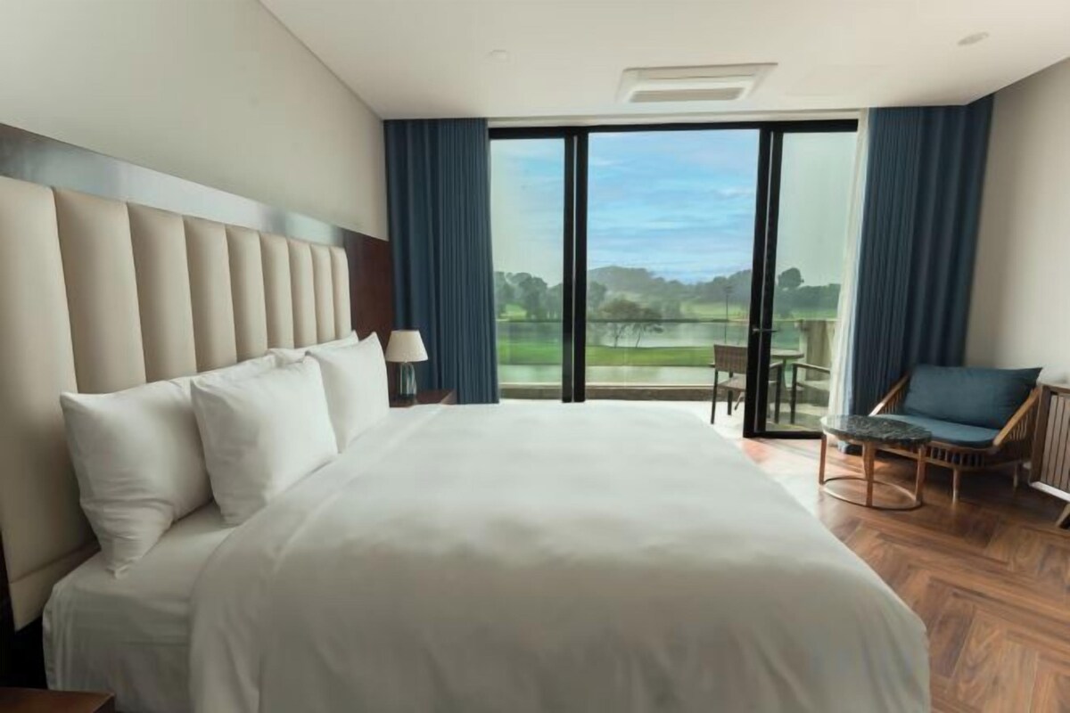 Quarto de hotel com uma cama grande, uma cadeira, uma mesa e vista pela porta de vidro.