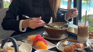 Une personne est assise à une table et déguste divers plats, notamment des œufs, des fruits et des pâtisseries.