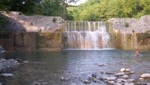Une piscine naturelle avec une cascade, entourée de murs de pierre et de verdure.