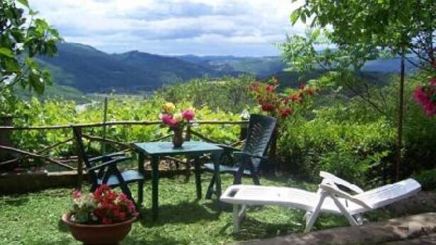 Une terrasse avec une table et des chaises, entourée d’une végétation luxuriante et dominée par un paysage montagneux.
