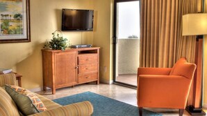 A hotel room with a sofa, a wooden cabinet, a television, a lamp, and a view through a sliding door. - Two Bedroom Condo, Ormond Beach, FL 1853114 (Ormond Beach)