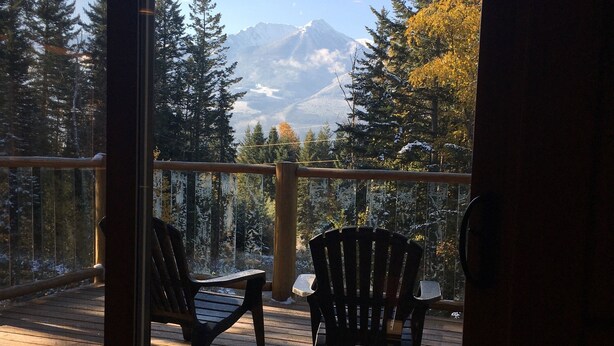 A wooden deck with two Adirondack chairs, a wooden railing, and a mountain view. - Golden Log House above the Valley (Golden)