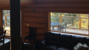 A cabin interior with a wooden deck, a black leather sofa, and a dining area. - Golden Log House above the Valley (Golden)