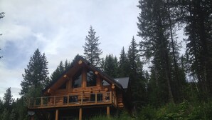 A wooden cabin with a balcony, surrounded by dense forest. - Golden Log House above the Valley (Golden)