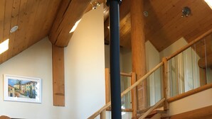 A wooden staircase with a glass railing leading to an upper level. A black stove is visible on the lower floor. - Golden Log House above the Valley (Golden)
