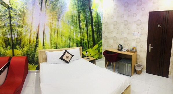 Ein Hotelzimmer mit Bett, Schreibtisch, Stuhl, kleinem Kühlschrank und einer Tür.