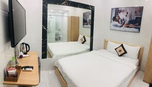 A hotel room with a bed, a desk with a telephone and a kettle, a mirror, and a picture on the wall.