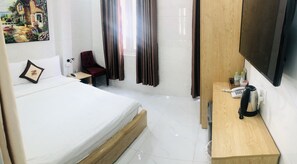 Ein Hotelzimmer mit einem Bett, einem Schreibtisch mit Telefon und Wasserkocher, einem Sessel und einem Bild an der Wand.