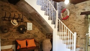 A rustic interior with a stone wall, a wooden bench with orange cushions, a large vase, and a white staircase. - Comfortable Fisherman's House (Llançà)