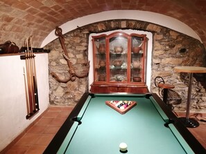 A billiards table in a room with stone walls, a wooden cabinet with glass doors, and a pool cue rack.