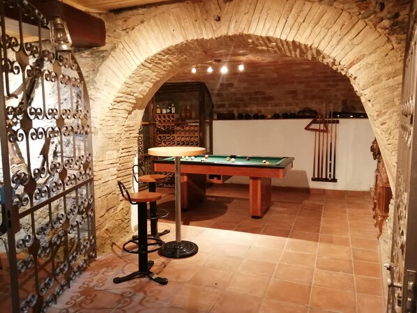 A billiards table in a room with a brick archway, a pool table, and a bar area with stools.