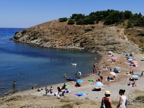 Une plage où des gens se prélassent au soleil et se baignent, entourée d’un paysage rocheux et d’arbres.