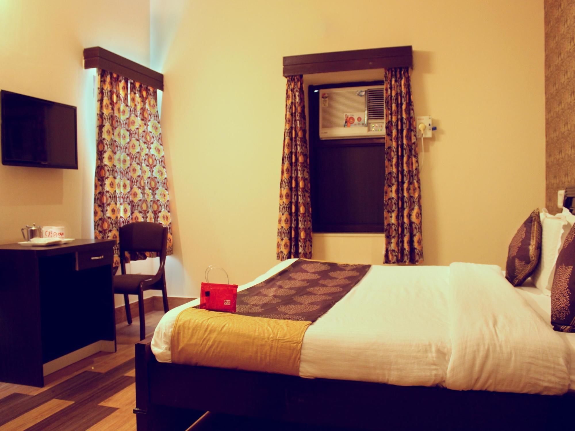 Een hotelkamer met een bed, bureau, stoel, televisie en airconditioning.