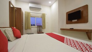 Une chambre d’hôtel équipée d’un lit, d’un téléviseur fixé au mur, d’un appareil de climatisation et d’une fenêtre avec des rideaux.