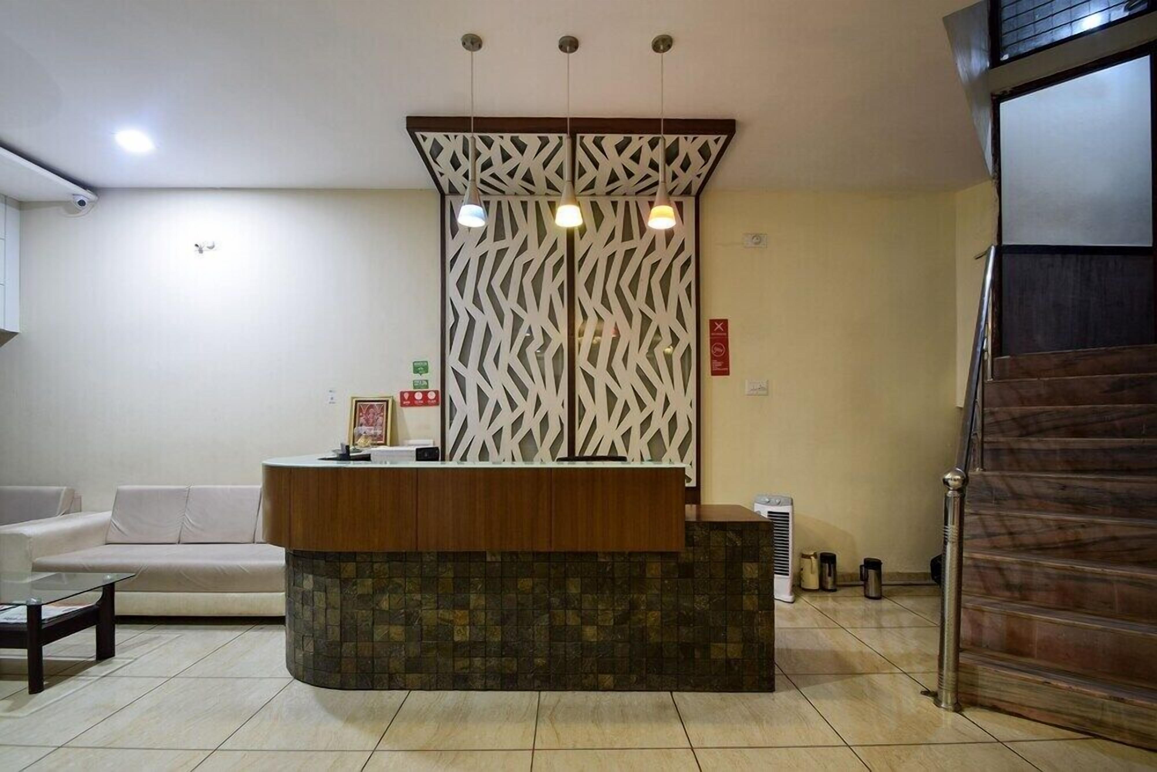 Una zona de recepción con un mostrador de madera, un separador decorativo, un sofá blanco y un suelo de baldosas.
