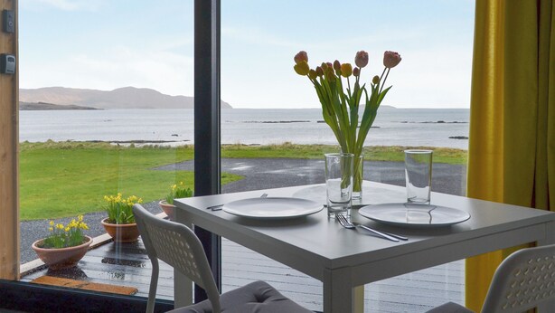 A dining table with plates, cutlery, and a vase of flowers. - The Isle View Nest - UK13547 (Lower Harrapool, near Broadford)