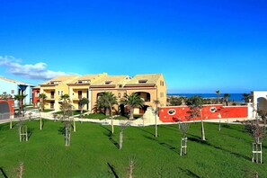 A large, multi-story hotel with a Mediterranean architectural style, featuring a central courtyard with palm trees and a view of the ocean.