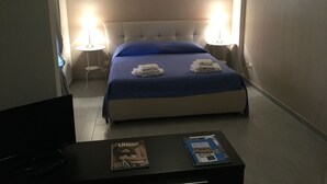A hotel room with a bed, two bedside lamps, a TV, and a magazine on a small table. - Open space apartment (Licata)