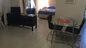 A hotel room with a bed, a desk, a glass dining table with chairs, and a window with curtains. - Open space apartment (Licata)