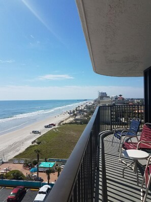 A balcony with a view of a beach and ocean, outdoor seating, and a parking area. - One Bedroom Ocean View Luxury Condo, Daytona Beach (1853132) (Daytona Beach)