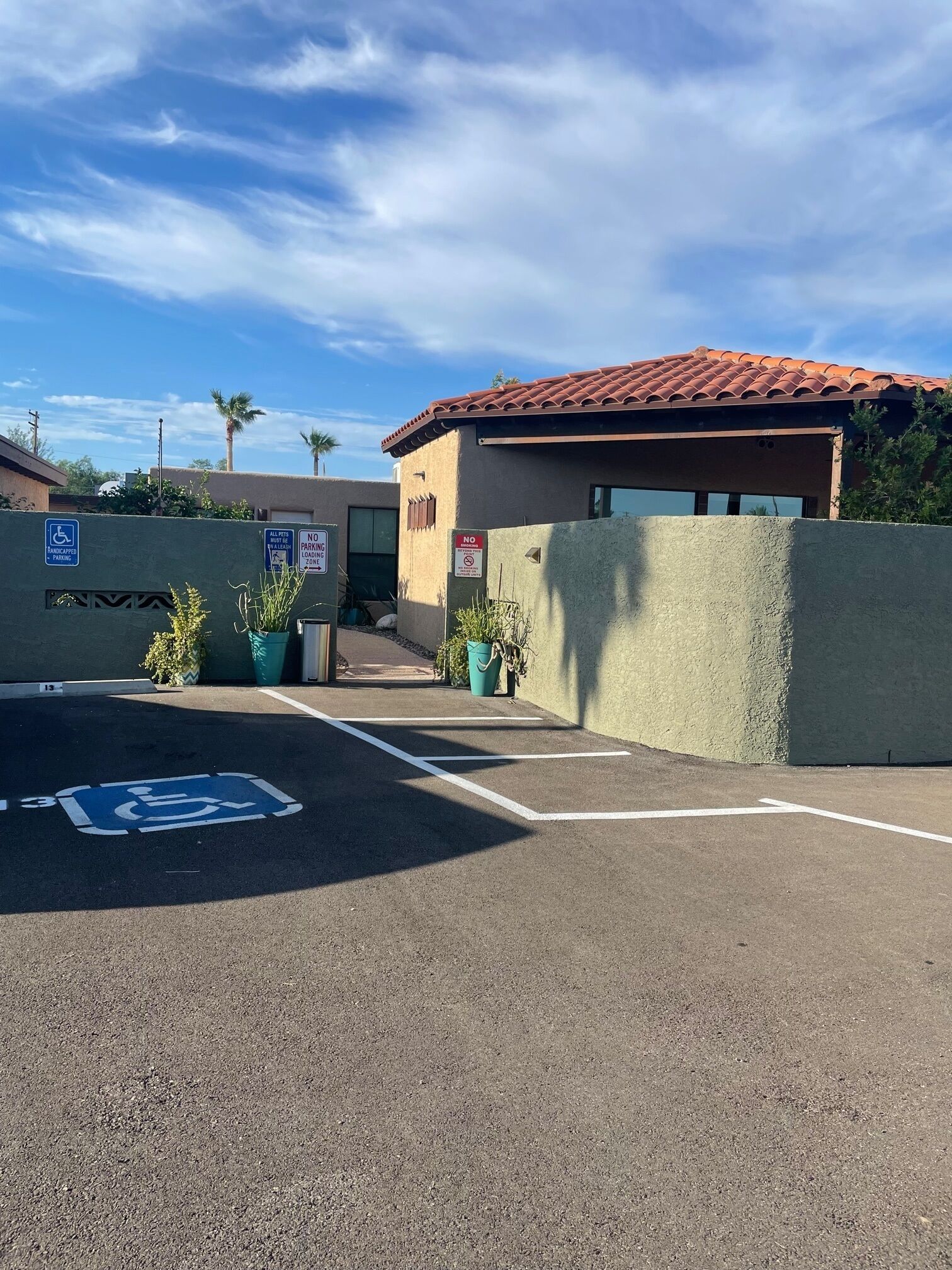 A parking lot with a handicapped parking space, a building with a red-tiled roof, and a sign indicating no parking.